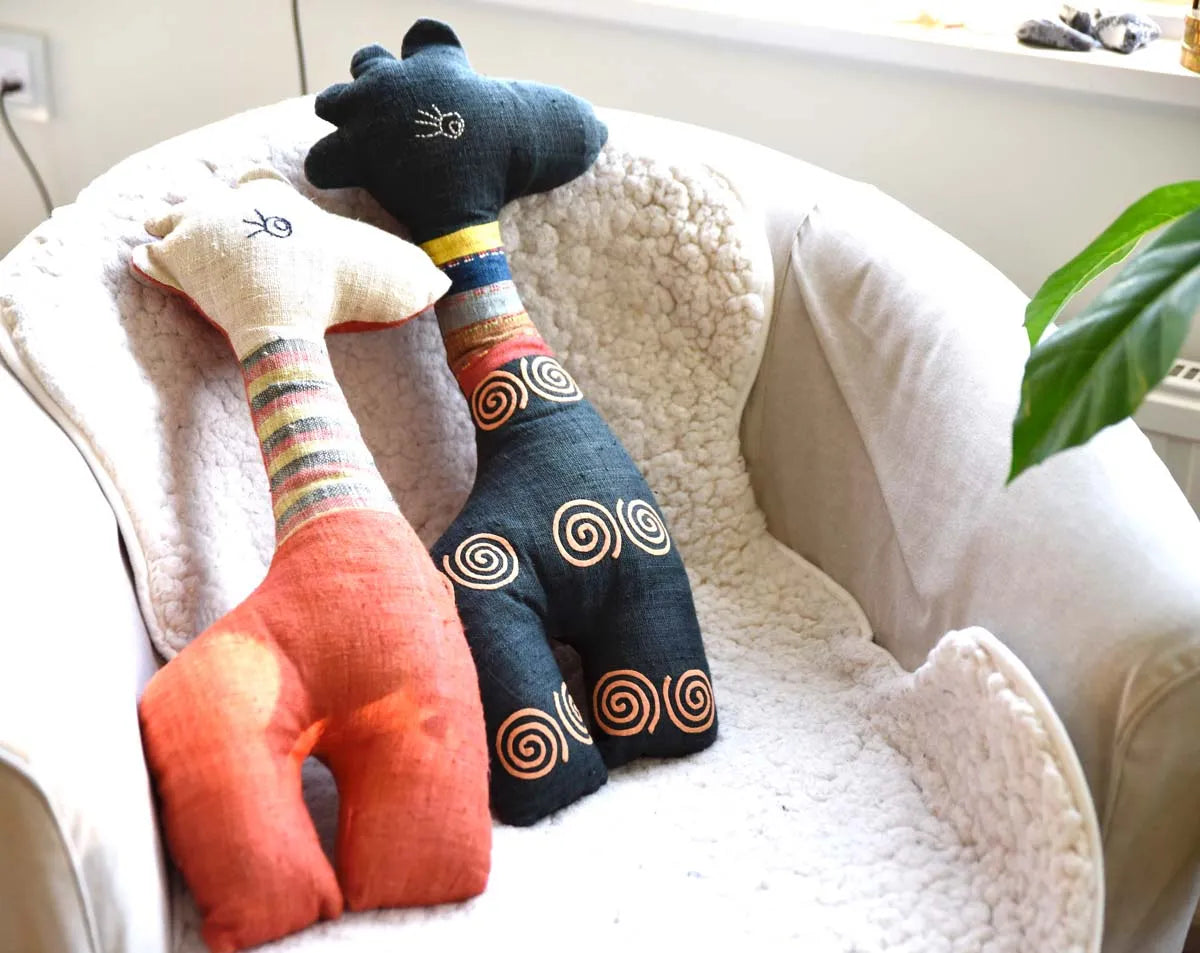 Two handmade deer plushies in orange and blue snuggled on sofa