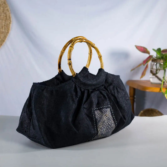 Black hemp handbag with bamboo handle, angled side view showing H’Mong patch, Purity Collection.