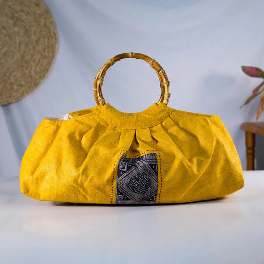 Yellow hemp handbag displayed on table, featuring bamboo handles and artisanal indigo patch detail.