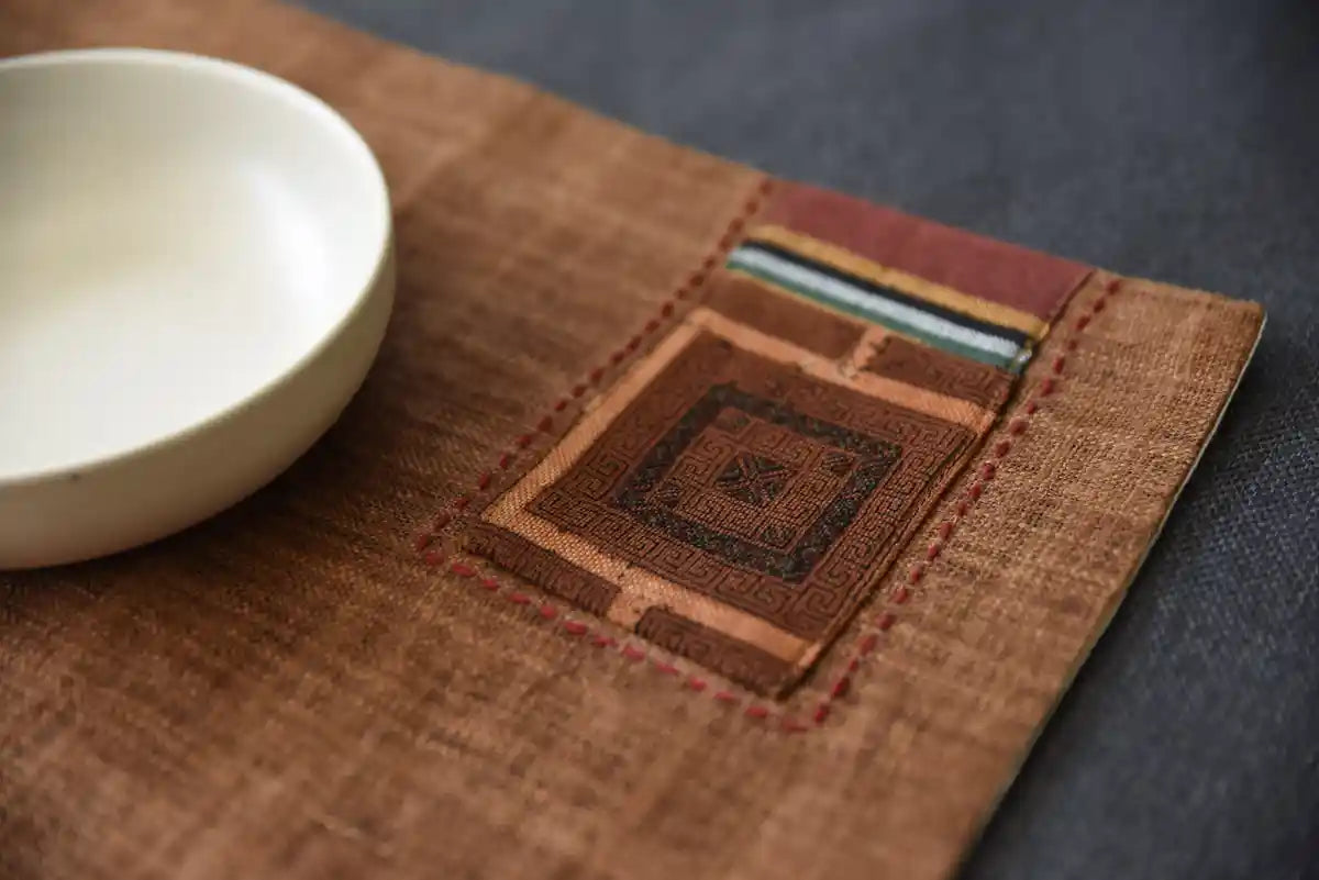 Närbild på brunt tygunderlägg med handsytt tribalmönster och blå kant