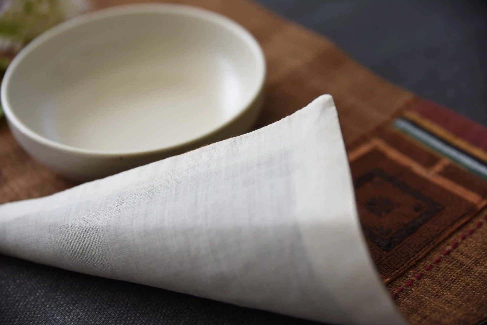 Linneunderlägg i brunt tyg med geometriskt tribalbroderi bredvid tallrik