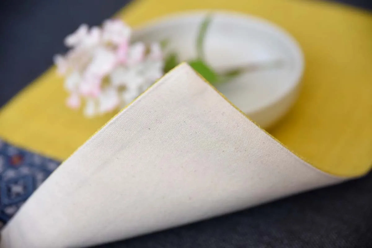 Folded edge of handmade yellow hemp placemat with indigo detail