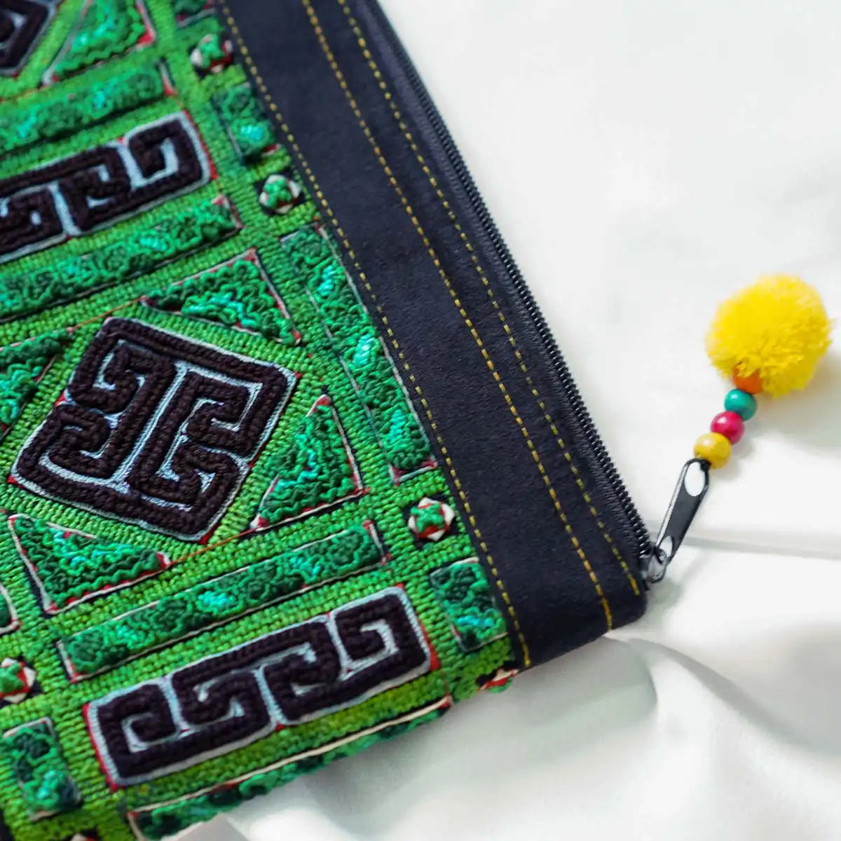 Close-up of green tribal embroidery on hemp clutch with yellow tassel